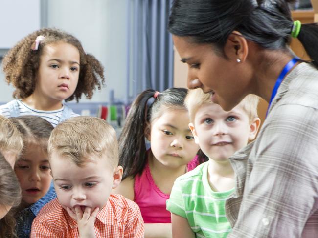 Female teacher giving a lesson to nursery students. They are sitting on the floor and there is a teacher taking notes.