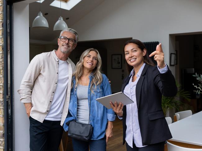 Real estate agent showing a house for sale to a couple and pointing outside - home ownership concepts