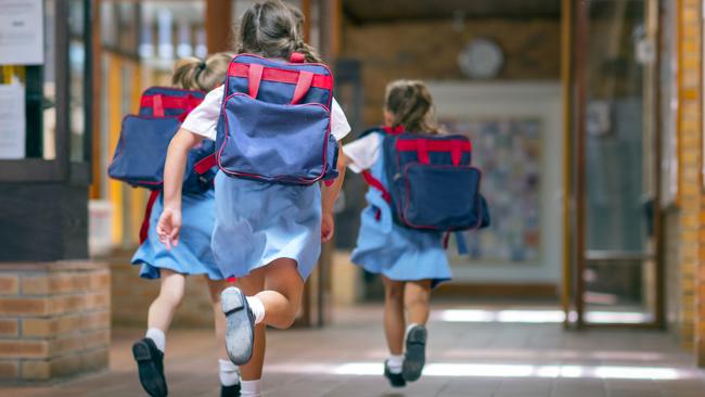 Rear view of excited students running towards entrance. Girls are carrying backpacks while leaving from school. Happy friends are wearing school uniforms. Source: iStock