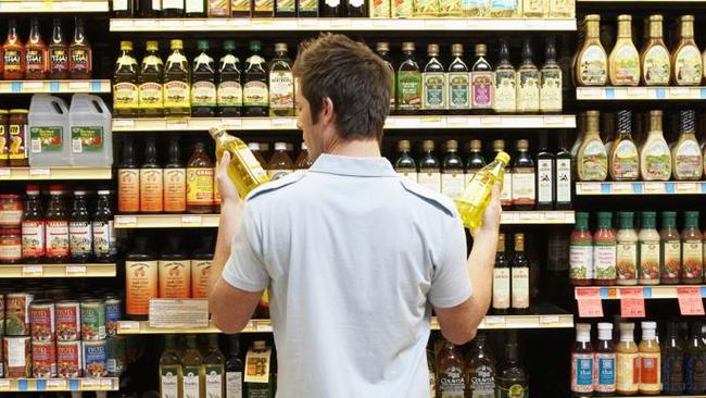 Young man in supermarket comparing bottles of oil, rear view, close-up