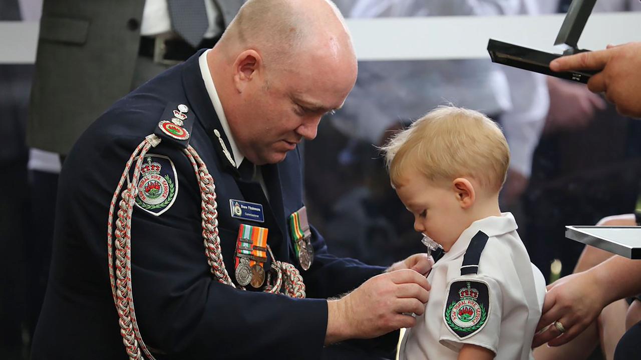 RFS Commissioner Shane Fitzsimmons (L) pins a medal on Harvey Keaton after his father Geoffrey Keaton was posthumously awarded with the Commissioner’s Commendation for Extraordinary Service and a Commendation for Bravery, at his funeral in Sydney. Picture: AFP