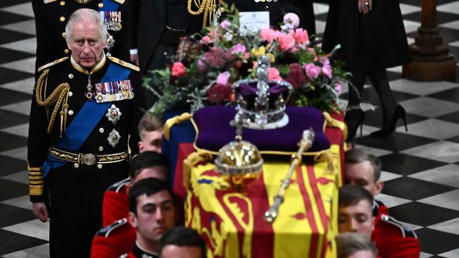 Britain's King Charles III walks beside the coffin of Queen Elizabeth II, draped in a Royal Standard and adorned with the Imperial State Crown and the Sovereign's orb and sceptre as it leaves the Abbey.