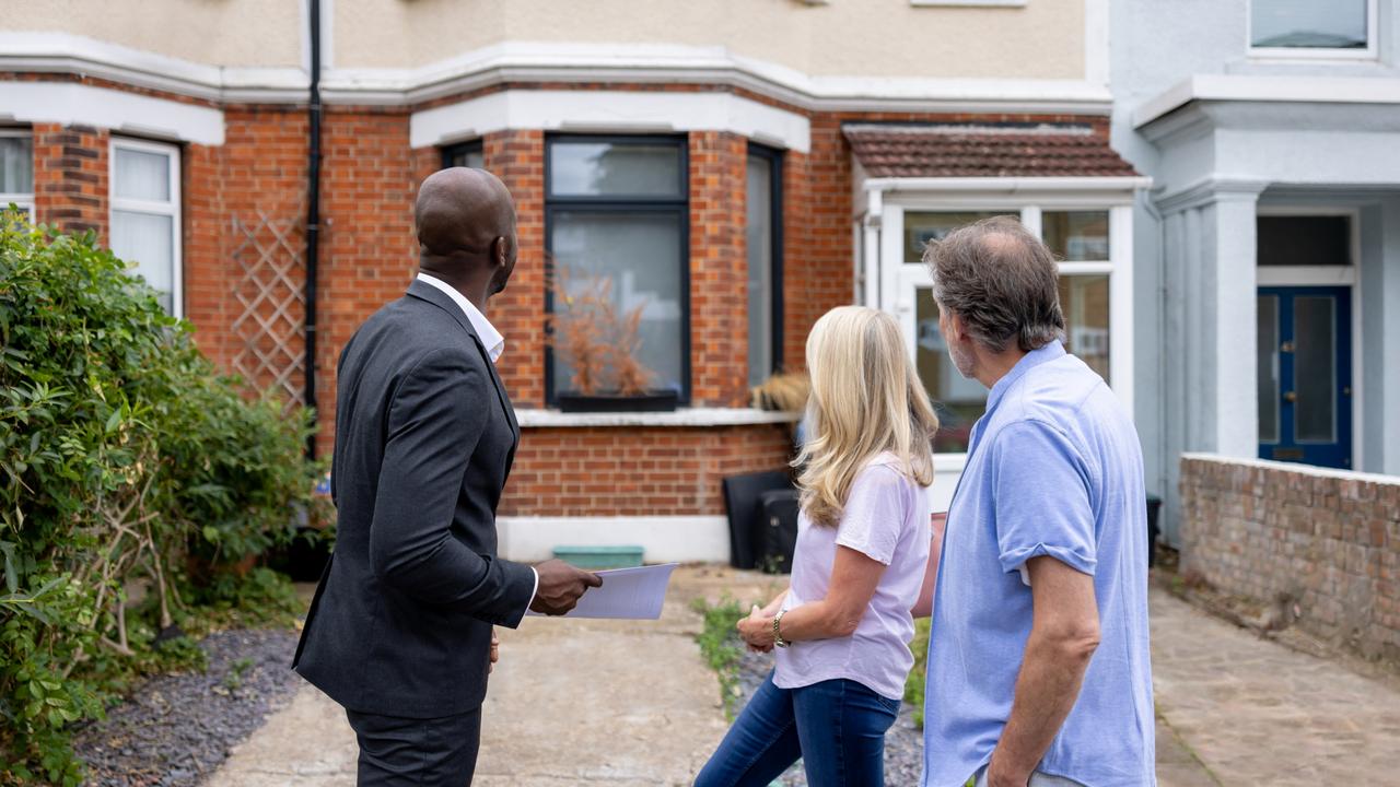 Overconfidence.  Couple looking at the front view of a house for sale with a real estate agent - home ownership concepts