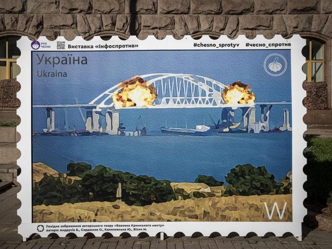 Ukrainians posed for photographs in front of a picture of a postage stamp in Kyiv showing an artists impression of the Kerch bridge on fire. Picture: Getty Images