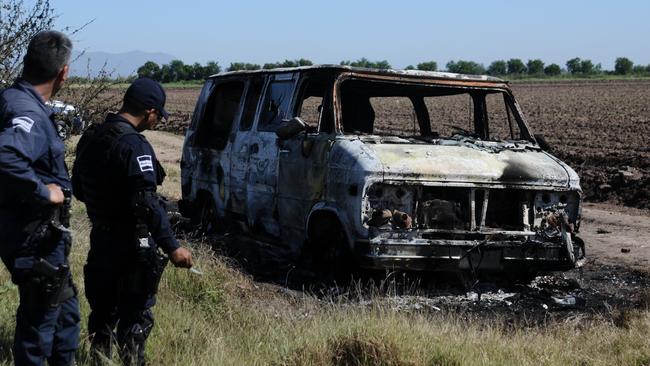 Destroyed ... Officers inspect the torched van of Adam Coleman and Dean Lucas, believed to have been targeted by drug cartel members. Picture: AFP