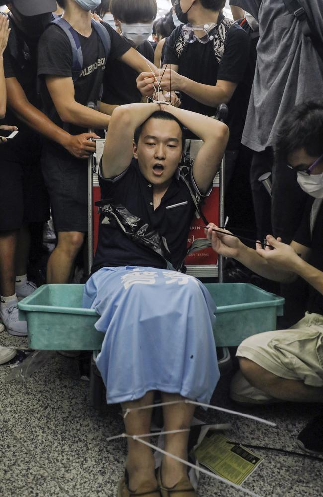 Protesters restrain a man on a luggage trolley, who protesters claimed was a Chinese undercover agent. Picture: AP