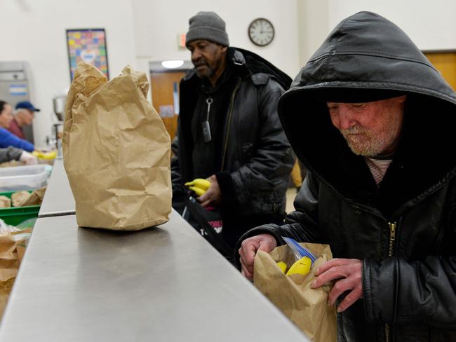 TOPSHOT - Guest receive their to-go meals in bagged lunch form at My Brother's Table soup kitchen in Lynn, Massachusetts on March 30, 2020. - With all restaurants ordered to shut down eating inside during the Coronavirus/Covid-19 pandemic, My Brother's Table, which also operates a shelter in the same building, is forced to have their guests eat their meals on the streets.  The kitchen, which serves an average of 600 meals a day, helps the homeless and anyone in need. (Photo by Joseph Prezioso / AFP)