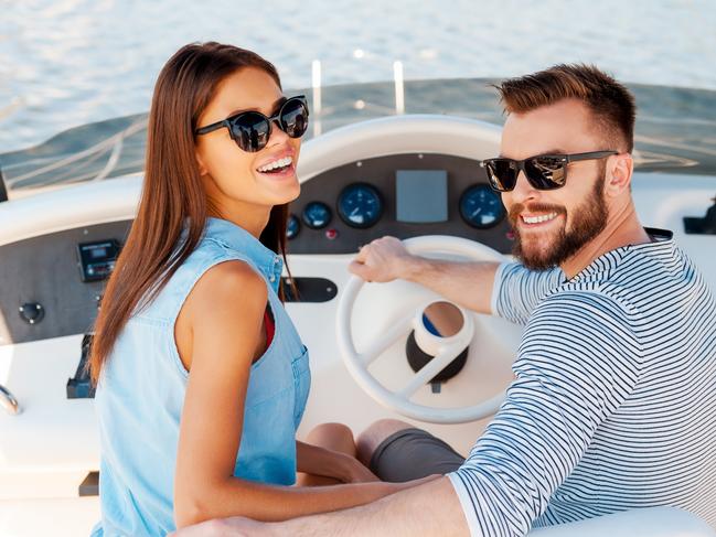 Cheerful young couple looking at camera and smiling while driving yacht. Boating generic.