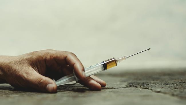 Human hand of a drug addict and a syringe with narcotic syringe lying on the floor.