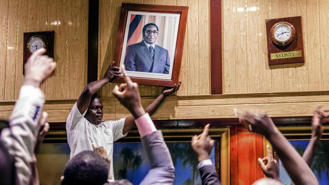 TOPSHOT - People remove, from the wall at the International Conference centre, where parliament had their sitting, the portrait of former Zimbabwean President Robert Mugabe after his resignation on November 21, 2017 in Harare. Robert Mugabe resigned as president of Zimbabwe on November 21, 2017 swept from power as his 37-year reign of brutality and autocratic control crumbled within days of a military takeover. The bombshell news was delivered by the parliament speaker to a special joint session of the assembly which had convened to impeach Mugabe, 93, who has dominated every aspect of Zimbabwean public life since independence in 1980.  / AFP PHOTO / Jekesai NJIKIZANA