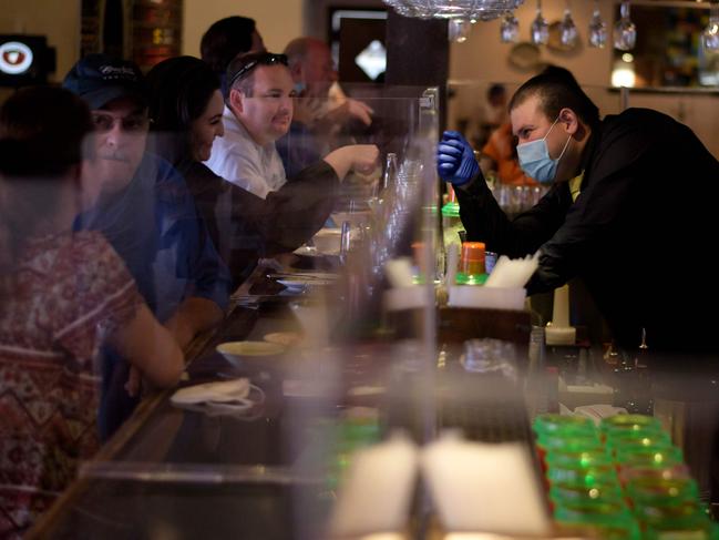 A bartender fist bumps a customer through a plastic barrier in Texas, which is the largest state to ease coronavirus lockdown measures. Picture: AFP