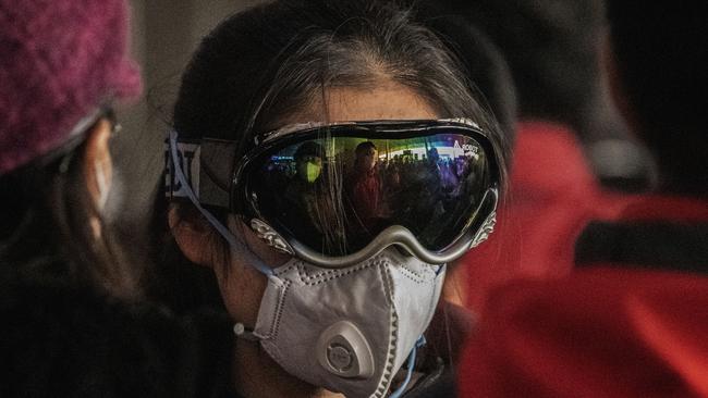 A woman wears a protective mask and ski goggles as she lines up to check in to a flight at Beijing Airport.