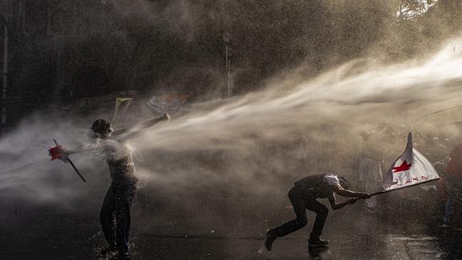 A leftist youth supporter fights against water cannons and tear gas attacks by the police while another tries to save the party flag during a demonstration in India against the ruling government, demanding education for all and youth employment. Picture: Dipayan Bose