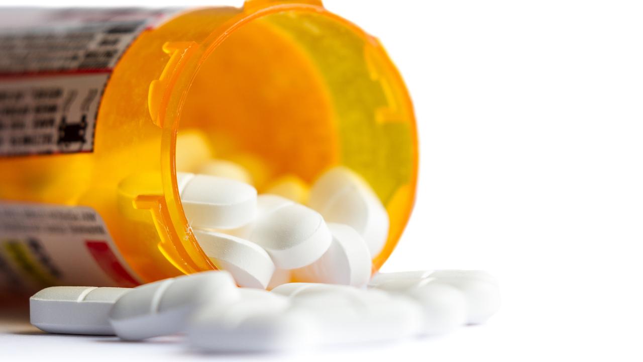 close up of a group of white tablets with an out of focus prescription bottle in the background