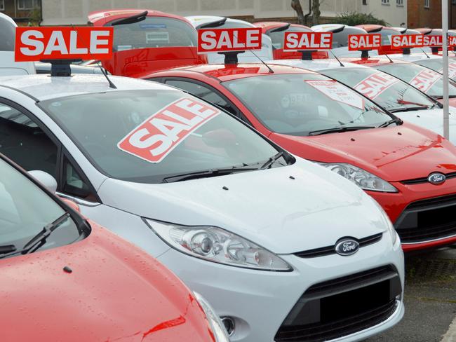 CARS GUIDE PICTURE: ALAMY Sale of used Ford cars on dealership forecourt outside showroom arranged alternate red and white obscured numberplates