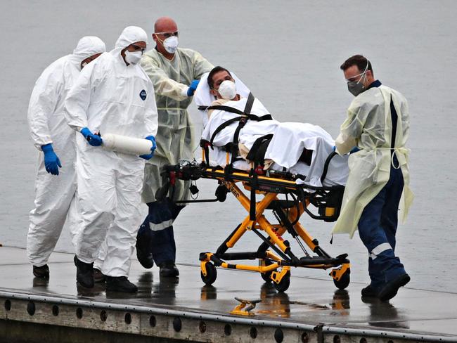 A Ruby Princess staff member being evacuated while surrounded by police and medical staff to an ambulance in Botany Bay. Picture: Adam Yip/The Australian