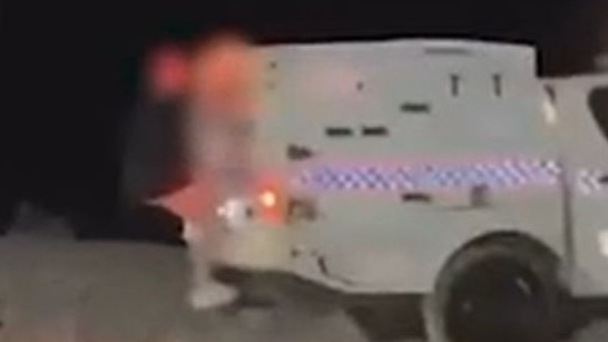 A teenager rides on the exterior of a police car at Schoolies on the Gold Coast in a screenshot from a social media video.