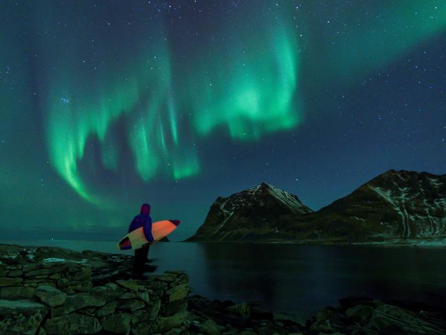 TOPSHOT - A surfer looks at Northern Lights on March 9, 2018 in Utakleiv, northern Norway, Lofoten islands, within the Arctic Circle.  / AFP PHOTO / OLIVIER MORIN