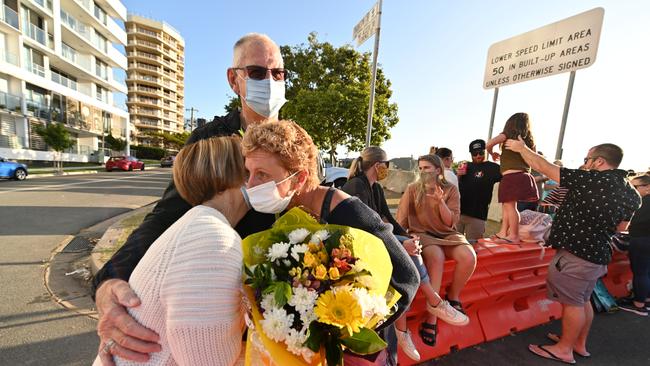 NSW mum Belinda Vardy gets hugs and flowers from her mother, Barbara Roberts, and father, Max, at the border barrier. As the lockdown hit, Ms Vardy was forced to travel to Queensland to support her son at school after her husband died and her other son committed suicide, and now she is stuck there.