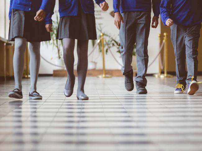 Cropped image of school kids in uniform walking together in a row through corridor. Focus on legs of students walking through school hallway.