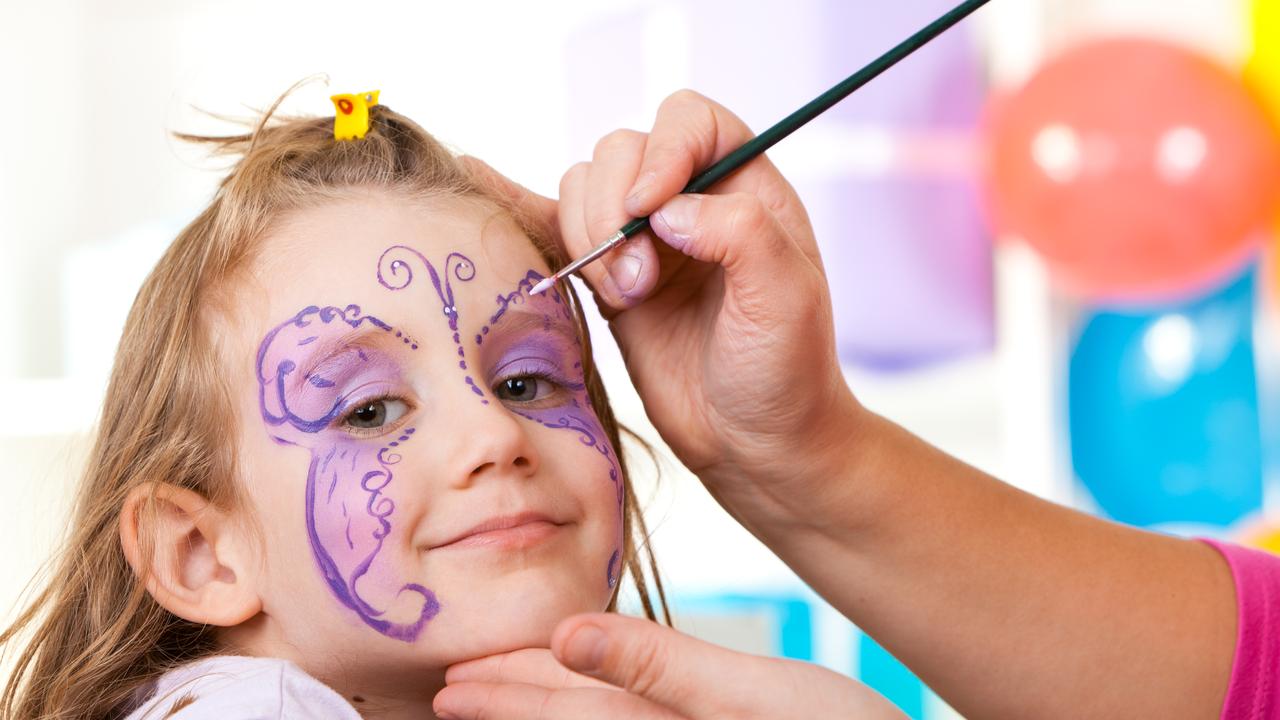 Little smiling girl having face painted on birthday party.