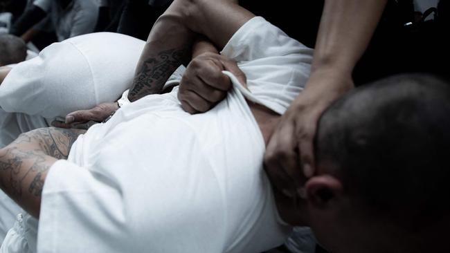 Prisoners’ heads are forced to the ground by officers. Picture: El Salvador’s Presidency Press Office/AFP