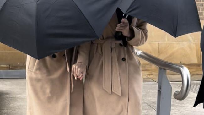 Grace and Lara Buttriss don matching outfits while hiding behind an umbrella exiting Picton Courthouse on August 19, 2022. Picture: Annie Lewis