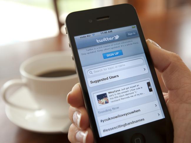 Female hand holding an iphone showing the Twitter sign up page. There is coffee on the dining table in the background.  This image shows the iphone being used in a casual environment.