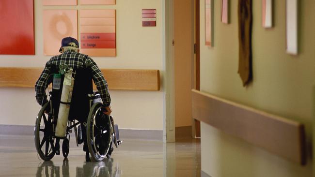 AGED CARE. Elderly man in hospital corridor in wheelchair, oxygen tank on back