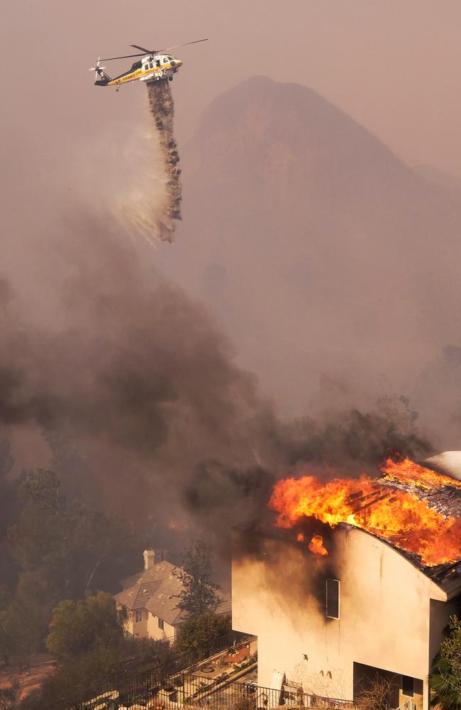 A helicopter drops water while a wildfire burns a home near Malibu Lake. Picture: AP Photo/Ringo H.W. Chiu