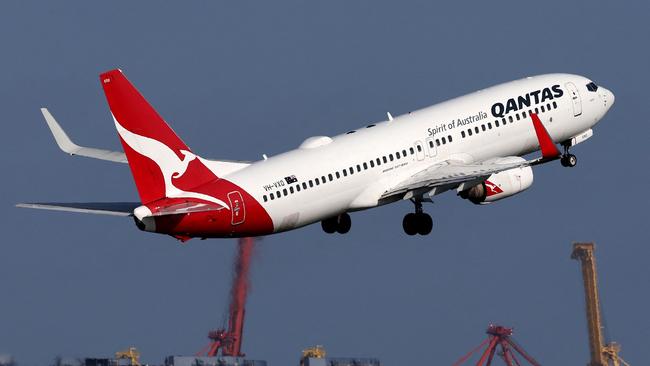 This picture taken on December 6, 2023 shows a Qantas Airways Boeing 737-800 passenger aircraft taking off at Sydneyâs Kingsford Smith international airport in front of a container ship berthed at the Port Botany container terminal. (Photo by DAVID GRAY / AFP)