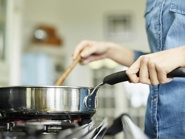 Midsection below view image of woman cooking food in pan. Utensil is placed on gas stove. Female is stirring dish in frying pan. She is preparing food in domestic kitchen.