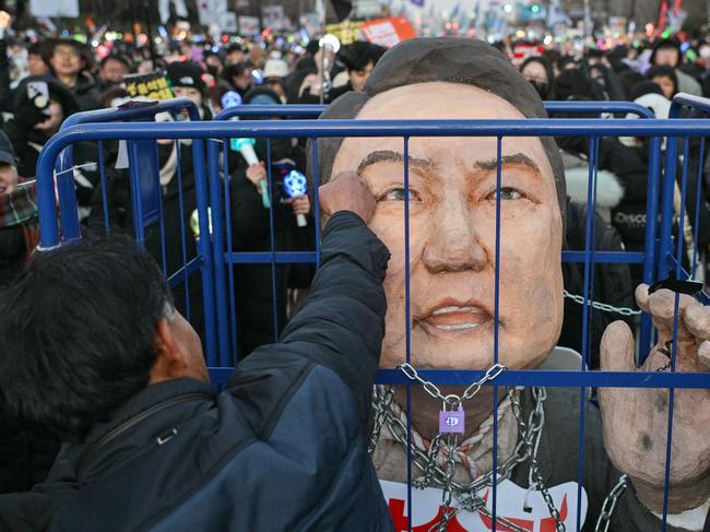 TOPSHOT - A protester calling for the ouster of South Korea President Yoon Suk Yeol punches an effigy of him after the result of the second martial law impeachment vote outside the National Assembly in Seoul on December 14, 2024. South Korean lawmakers on December 14 voted to remove President Yoon Suk Yeol from office for his failed attempt to impose martial law last week. (Photo by ANTHONY WALLACE / AFP)