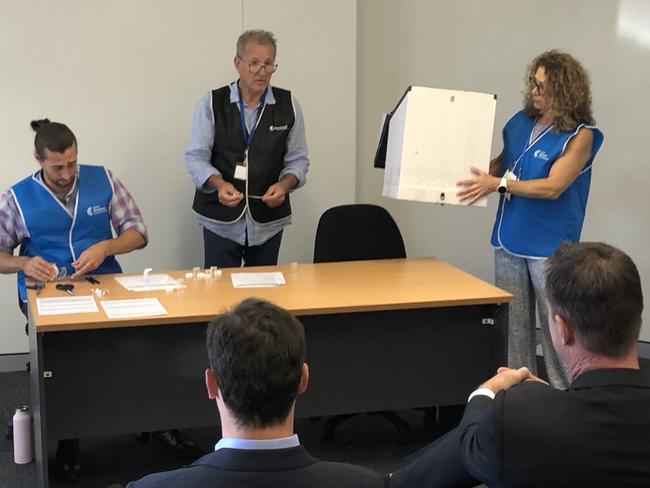 The NSW Electoral Commission's Wakehurst election manager, Ron Krueger (centre), makes the ballot draw for the seat of Wakehurst on Thursday, to decide the order of candidates on the ballot paper for the March 25 state election as Liberal candidate Toby Williams (front, left) and independent candidate Michael Regan, look on. Picture: Jim O'Rourke