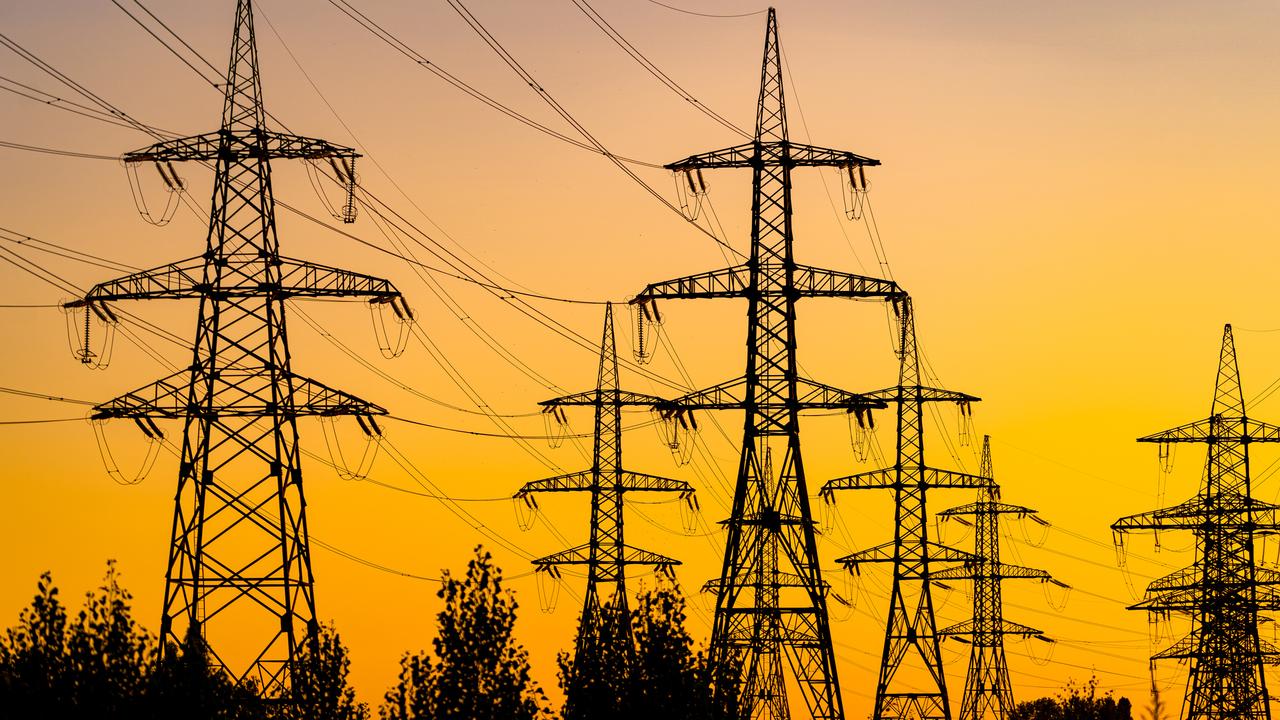 Power pylons reache into the sunset sky. Silhouettes of big trees under energy transmission towers.