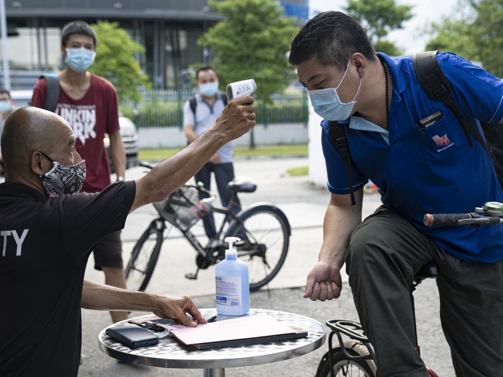 A migrant worker wearing protective face mask has his temperature checked by a security guard before entering a factory-converted dormitory in Singapore. Picture: Getty