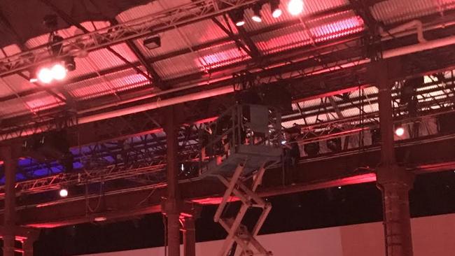 Guests mingle below while police use a hoist to talk to coal mining protester chained to scaffolding above the stage.