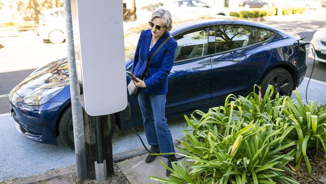 A Tesla owner connects her vehicle a white kerbside charging pod.