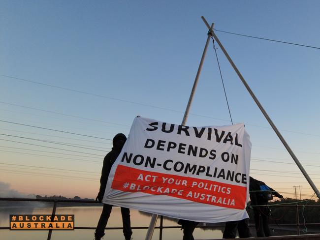 Ian Fox from Adelaide, age 67, has climbed atop the Kooragang Rail Bridge and suspended himself over the Hunter River, blocking all rail in and out of the Port of Newcastle, the world’s largest coal port. , , He holds a banner which reads: “Survival depends on non-compliance. Act your politics.” , Ian is a representative of the activist network called Blockade Australia. Picture: Blockade Australia