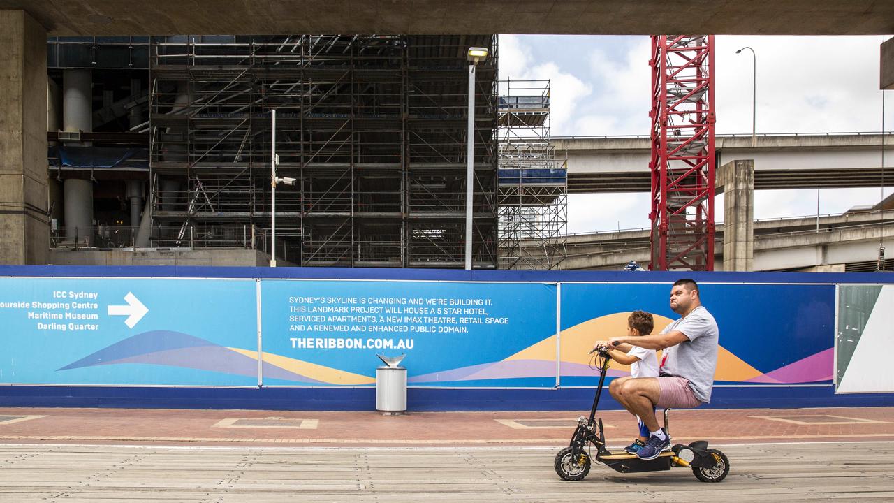 A man and child are seen riding past signage advertising the Ribbon project at Darling Harbour. Picture: Jenny Evans/NCA NewsWire