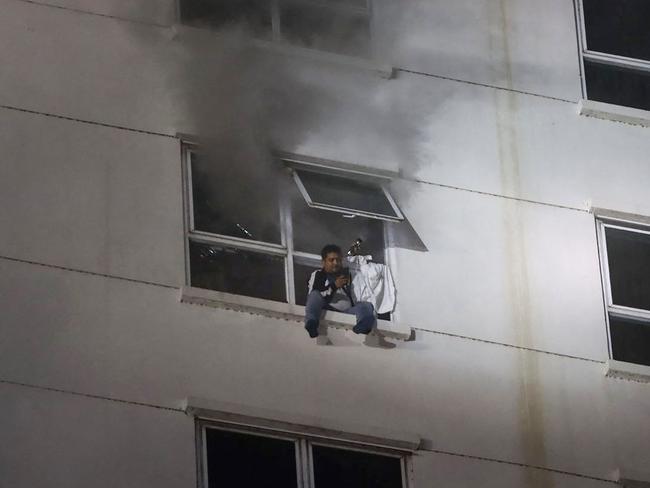 A man sits on a window ledge as a fire burns through the Grand Diamond City hotel-casino in Poipet on December 29, 2022. Picture: AFP.