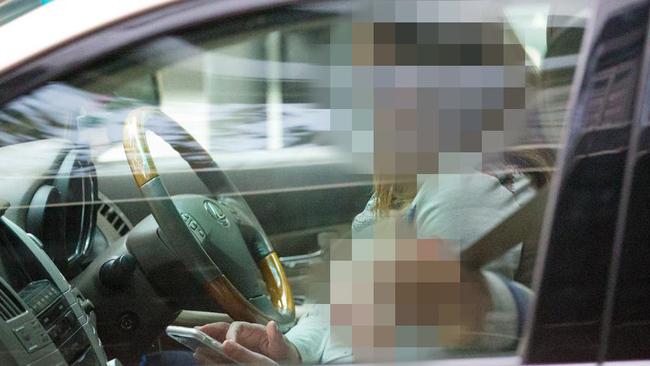 A woman using her phone while stopped at a red light with a child in the front passenger seat. Picture: Mark Stewart