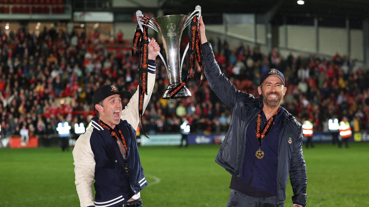 WREXHAM, WALES - APRIL 22: Wrexham owners Rob McElhenney and Ryan Reynolds hold the Vanarama National League Trophy as Wrexham celebrate promotion back to the English Football League during the Vanarama National League match between Wrexham and Boreham Wood at Racecourse Ground on April 22, 2023 in Wrexham, Wales. (Photo by Matthew Ashton - AMA/Getty Images)