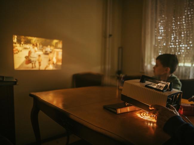 Grandfather and grandson sitting at the table and looking photos on vintage slide projector at elderly man's home.