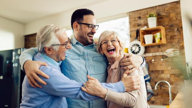 Cheerful mid adult man and his senior parents laughing while embracing in the kitchen. happy retirees generic retirement