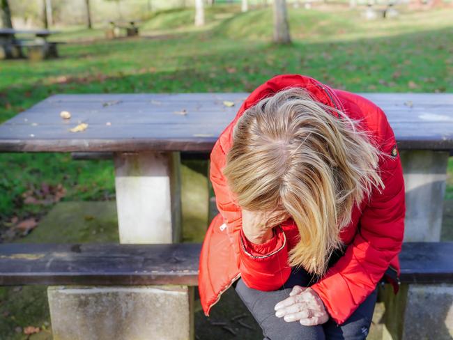 A woman with her head down sad and depressed in a park. World suicide prevention day.