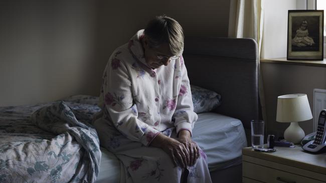 BAD AGED CARE: A shot of a senior woman sitting on the side of her bed with her head down looking sad. She looks like she has just woken up as is dressed in nightwear.