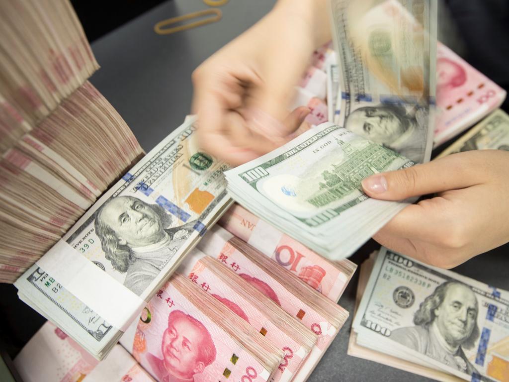 A Chinese bank employee counts 100-yuan notes and US dollar bills at a bank counter in Nantong in China’s eastern Jiangsu province. Picture: STR/AFP