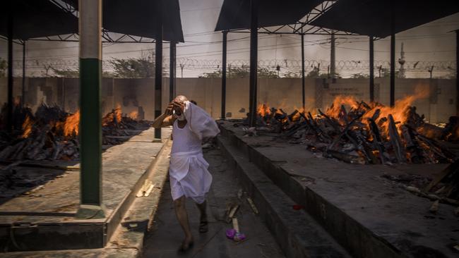 A priest who helps performing last rites, runs while covering his face amid the multiple burning funeral pyres of COVID-19 patients in New Delhi, India. Picture: Getty Images