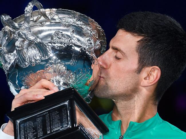 (FILES) This file photo taken on February 21, 2021 shows Serbia's Novak Djokovic kissing the Norman Brookes Challenge Cup trophy following his victory against Russia's Daniil Medvedev in the men's singles final on day 14 of the Australian Open tennis tournament in Melbourne. - Novak Djokovic was listed for a night match on January 17, 2022 to open his Australian Open title defence, as he awaited a court decision on his appeal against deportation. (Photo by William WEST / AFP) / TO GO WITH AFP STORY Tennis-AUS-Open-men-five -- IMAGE RESTRICTED TO EDITORIAL USE - STRICTLY NO COMMERCIAL USE --